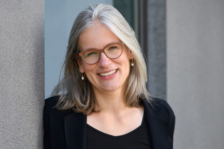 Gesundheitspsychologin Prof. Dr. Jutta Mata lehnt an eine Betonwand und lächelt. Sie trägt einen schwarzen Blazer und ein schwarzes T-Shirt.