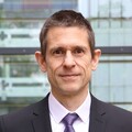 Martin Schlather hat kurze braune Haare. Er trägt einen schwarzen Anzug und eine lilane Krawatte.
