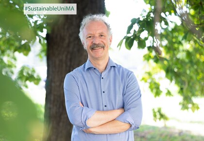 Prof. Dr. Moritz Fleischmann. Er lächelt, sein Hemd ist hellblau gestreift und er hat einen Schnurrbart.