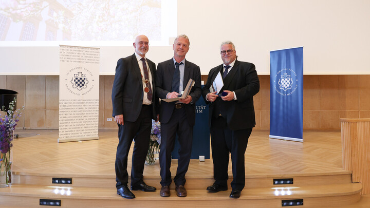 Professor Dr. Thomas Puhl, Professor Dr. Thomas König und Michael Meckel stehen am Universitätstag in der Aula des Schlosses und lächeln in die Kamera.