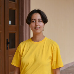 Fine Giebler wears a yellow shirt and stands in an entrance hall of the Schloss.