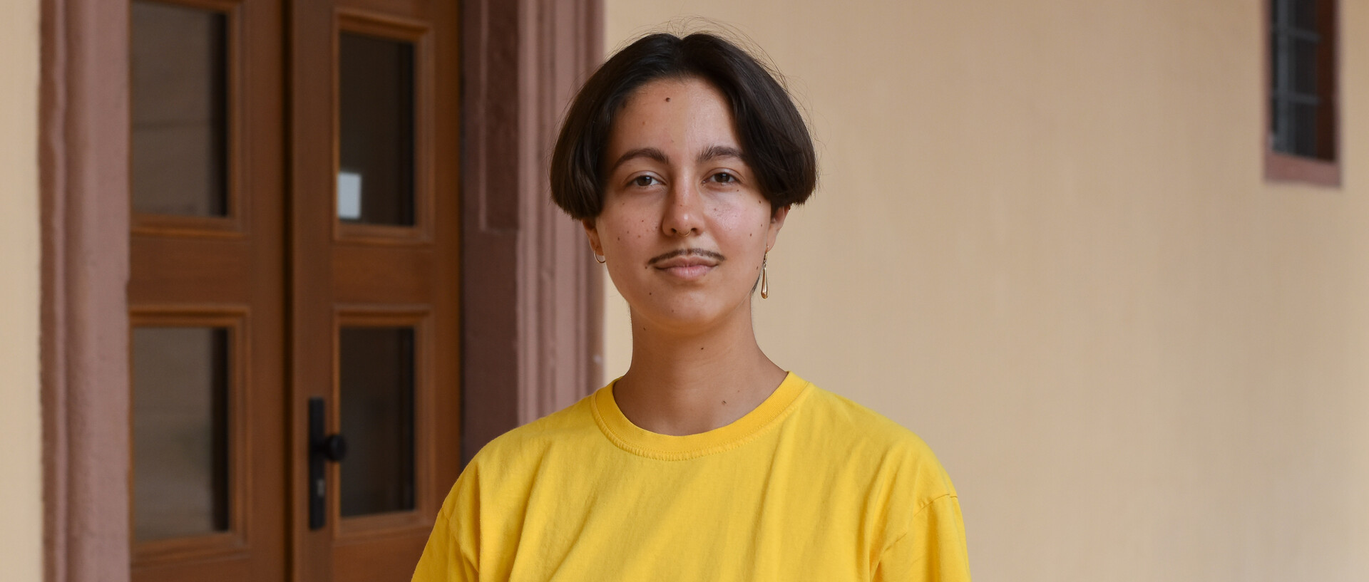 Fine Giebler wears a yellow shirt and stands in an entrance hall of the Schloss.