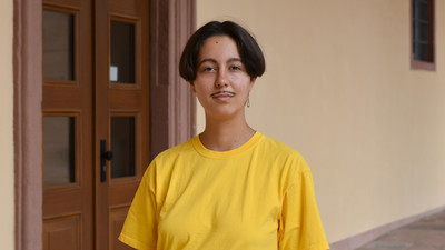 Fine Giebler wears a yellow shirt and stands in an entrance hall of the Schloss.