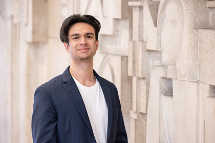 Porträt von Virgil Baclanoc. Er steht vor einer Wand, hat schwarze kurze Haare und trägt ein dunkelblaues Jackett.