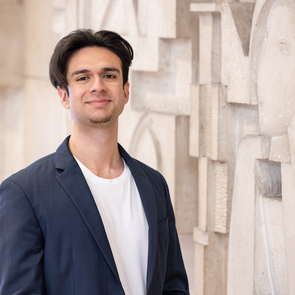 Porträt von Virgil Baclanoc. Er steht vor einer Wand, hat schwarze kurze Haare und trägt ein dunkelblaues Jackett.