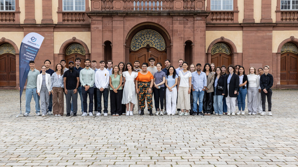 Eine Gruppe junger Menschen steht vor dem Mannheimer Schloss und posiert für ein Gruppenfoto.
