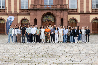 Eine Gruppe junger Menschen steht vor dem Mannheimer Schloss und posiert für ein Gruppenfoto.
