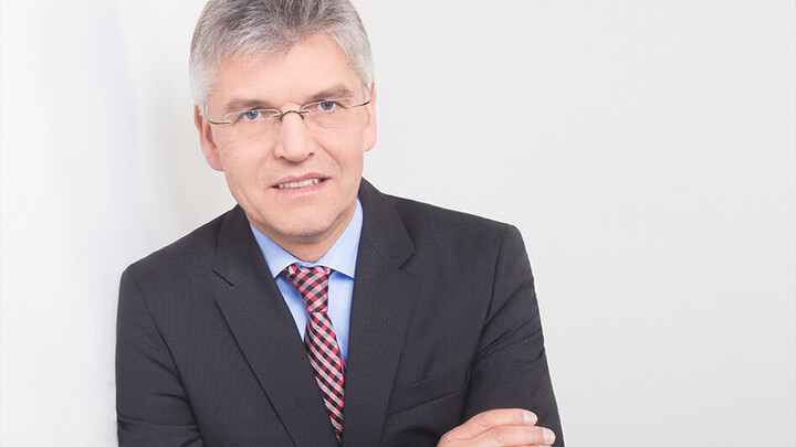 Portrait von Christoph Spengel. Er trägt ein schwarzes Jackett und lehnt an eine weiße Wand.