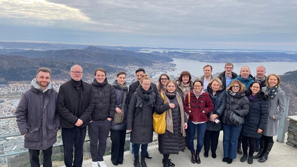 Eine Gruppe von Menschen steht auf einer Aussichtsplattform. Im Hintergrund sind Berge.