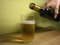 Ein Trinkglas, in das Bier eingeschenkt wurde. Die Bierflasche wird daneben gehalten.