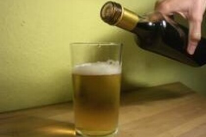 Ein Trinkglas, in das Bier eingeschenkt wurde. Die Bierflasche wird daneben gehalten.