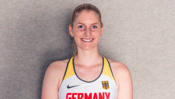 Lisa Nippgen steht Lächelnd vor einer grauen Wand. Sie trägt ein graues Leichtathletik-Trikot.