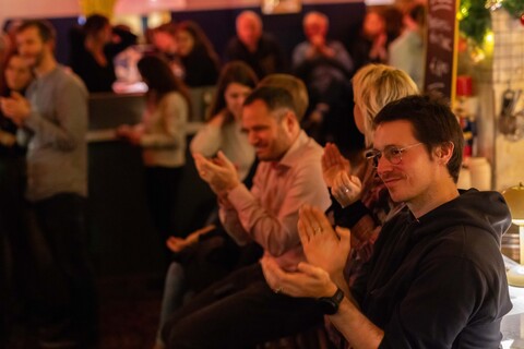 Mehrere Personen sitzen in einer Bar und klatschen.