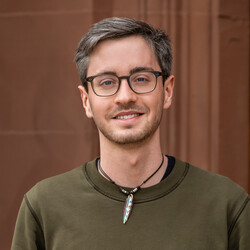 Jan Koterzyna. Die Person trägt einen grünen Pullover und lächelt freundlich in die Kamera