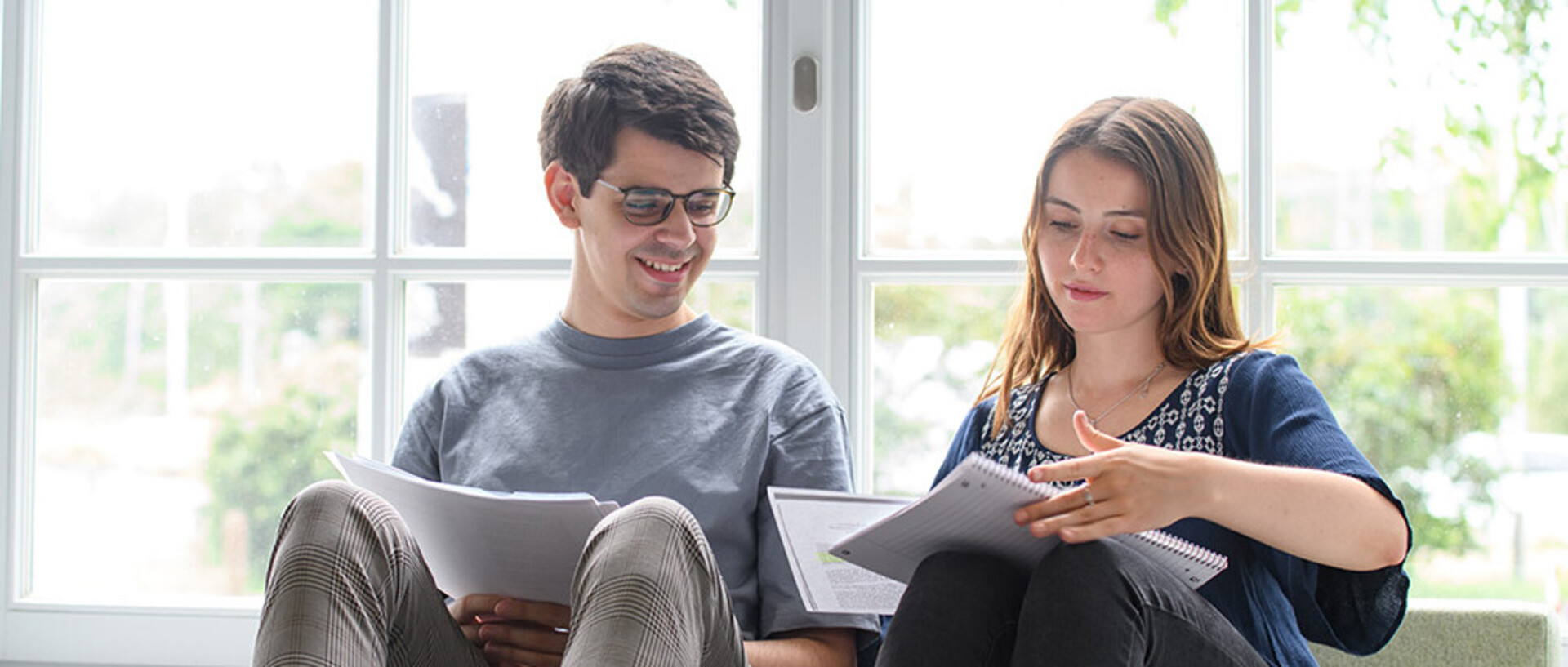Ein Student und eine Studentin sitzen am Fenster und betrachten ein Vorlesunsskript
