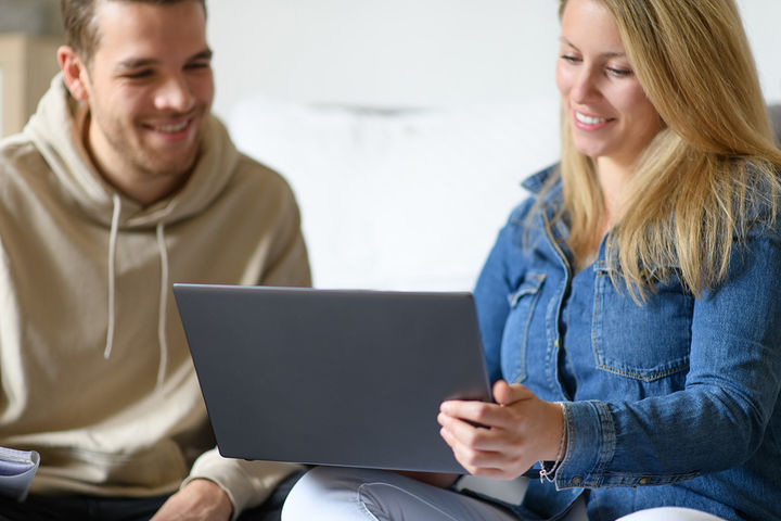 Eine junge Frau zeigt einem jungen Mann etwas auf dem Laptop.