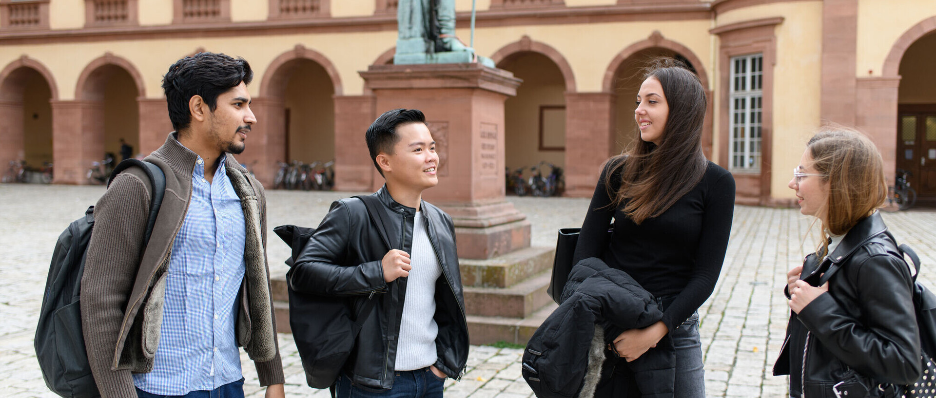 Eine Gruppe Studierende steht im Ehrenhof des Schlosses. Sie unterhalten sich. Im Hintergrund sieht man Teile einer Statue.
