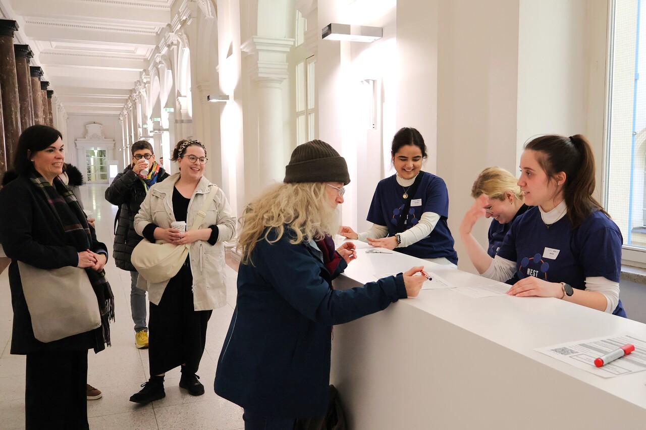Teilnehmende melden sich bei den Hifskräften zur Tagung an, es herrscht fröhliche Stimmung.