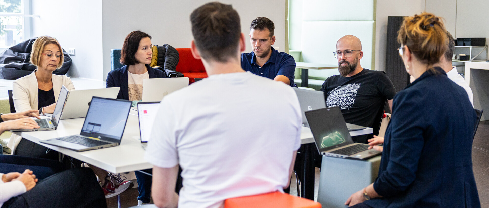 KI-Kernteam Neun Mitarbeitende sitzen gemeinsam an einem großen Tisch. Vor ihnen liegen aufgeklappte Laptops.