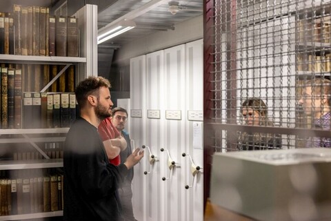 Personen in Universitätsbibliothek mit historischen Sammlungen. Im Hintergrund viele alte braune Bücher.