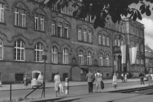 schwarz-weiß Aufnahme des Haupteingangs der Wirtschaftshochschule. Viele Studierende stehen davor. 