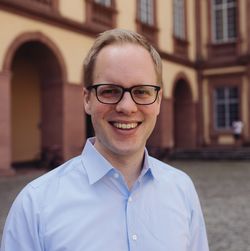 Jens Brandenburg hat kurze blonde Haare und eine Brille. Er trägt ein hellblaues Hemd.