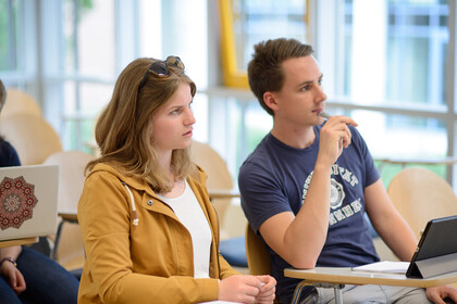 Zwei Studierende sitzen nebeneinander. Sie schauen konzentriert nach vorne.