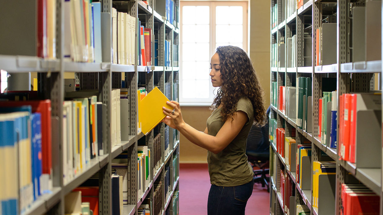 Eine Studentin zieht ein gelbes Buch aus einem Regal in der Bibliothek.