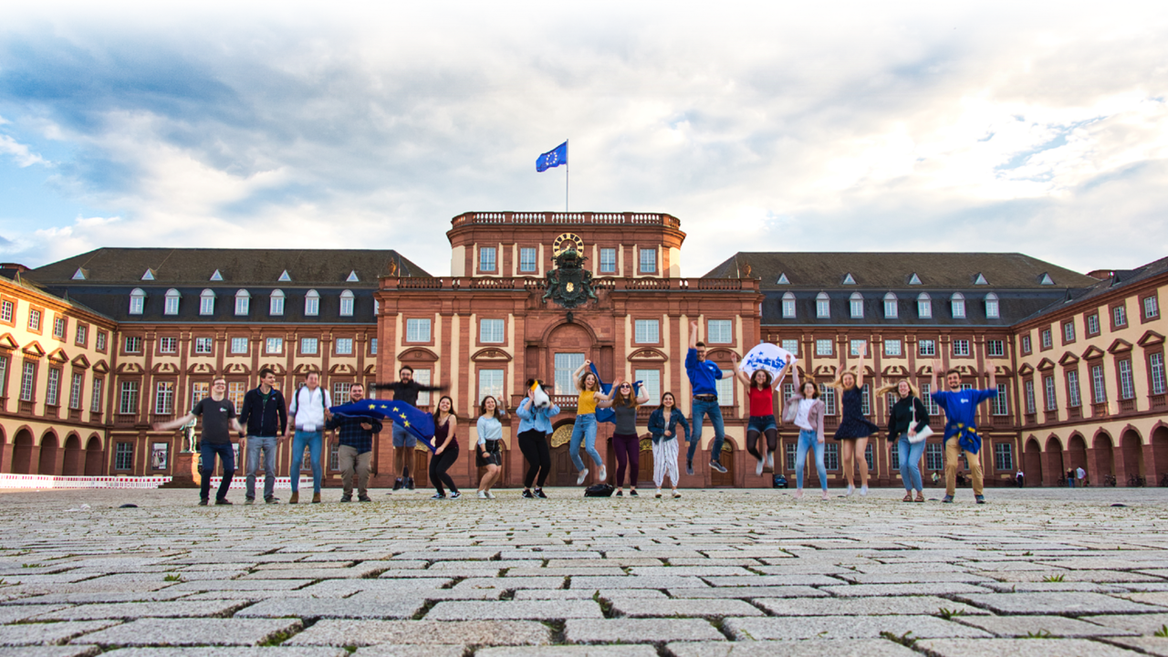Studierende springen vor dem Mannheimer Schloss hoch.
