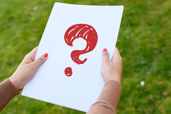Symbolbild. Eine Person mit rot lackierten Fingernägeln hält ein weißes Blatt Papier. Auf dem Papier ist ein rotes Fragezeichen eingezeichn0et.