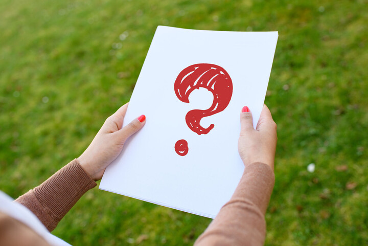 Symbolbild. Eine Person mit rot lackierten Fingernägeln hält ein weißes Blatt Papier. Auf dem Papier ist ein rotes Fragezeichen eingezeichn0et.