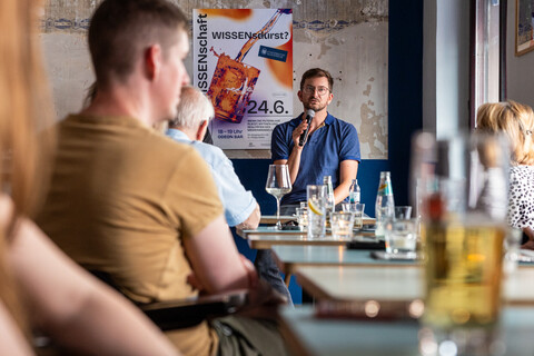 Mann mit Mikrofon spricht bei Wissenschaftsveranstaltung in einer Bar.