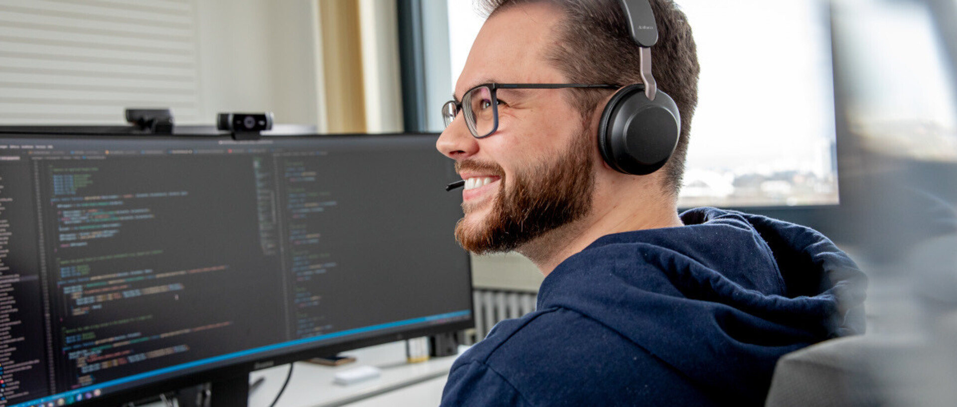 Ein Mitarbeiter mit Headphone sitzt vor einem sehr breiten Bildschirm.