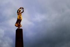 Eine Frau in gelbem Gewand steht auf einem Turm und hält einen Ring in die Höhe.