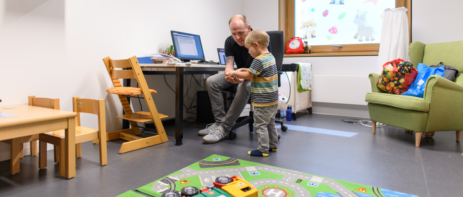 Vater und Sohn sitzen in einem Spielraum, der Vater zeigt dem Sohn etwas.