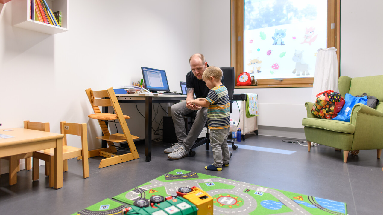 Vater und Sohn sitzen in einem Spielraum, der Vater zeigt dem Sohn etwas.