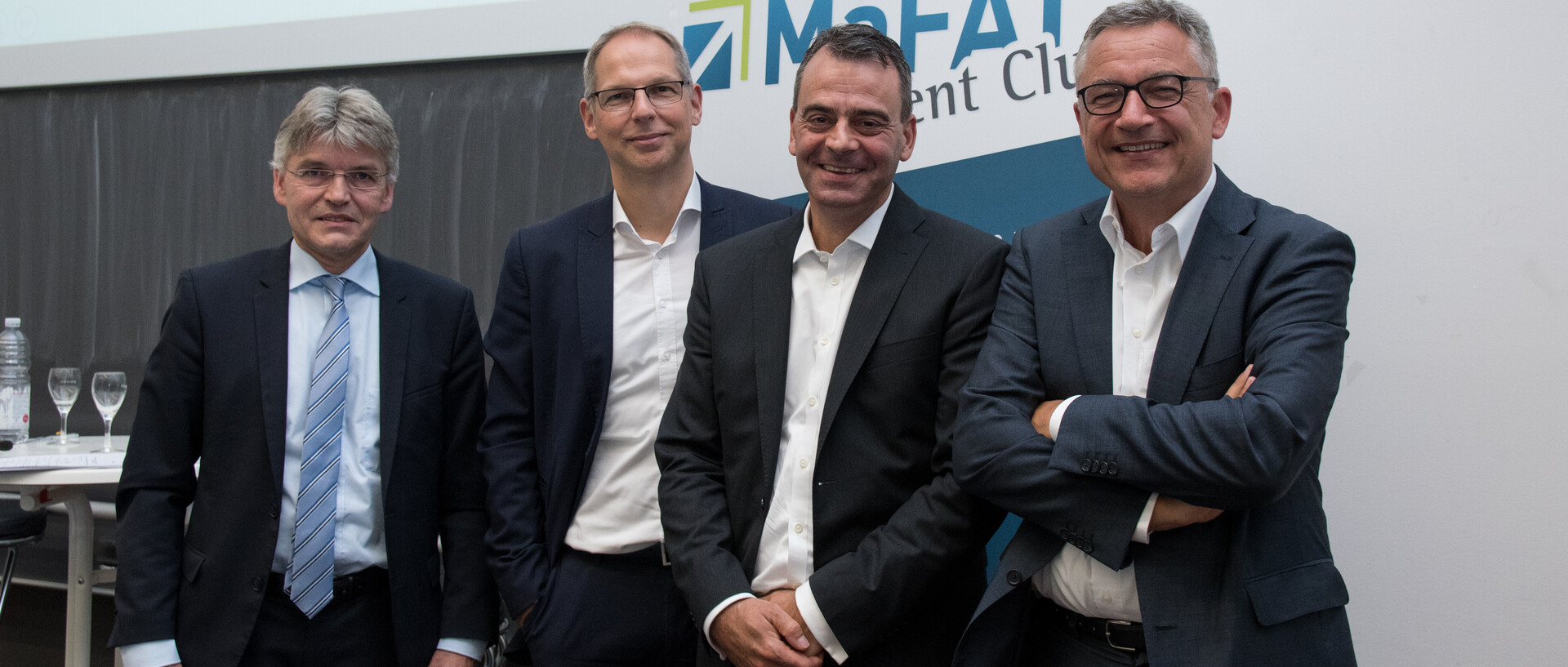 Vier Männer in Anzügen stehen vor einem Rollup mit der Aufschrift "MaFAT". 