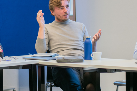 Filippo Bontadini trägt einen grauen Pullover und sitzt an einem Tisch. Er gestikuliert mit seinen Händen und spricht.