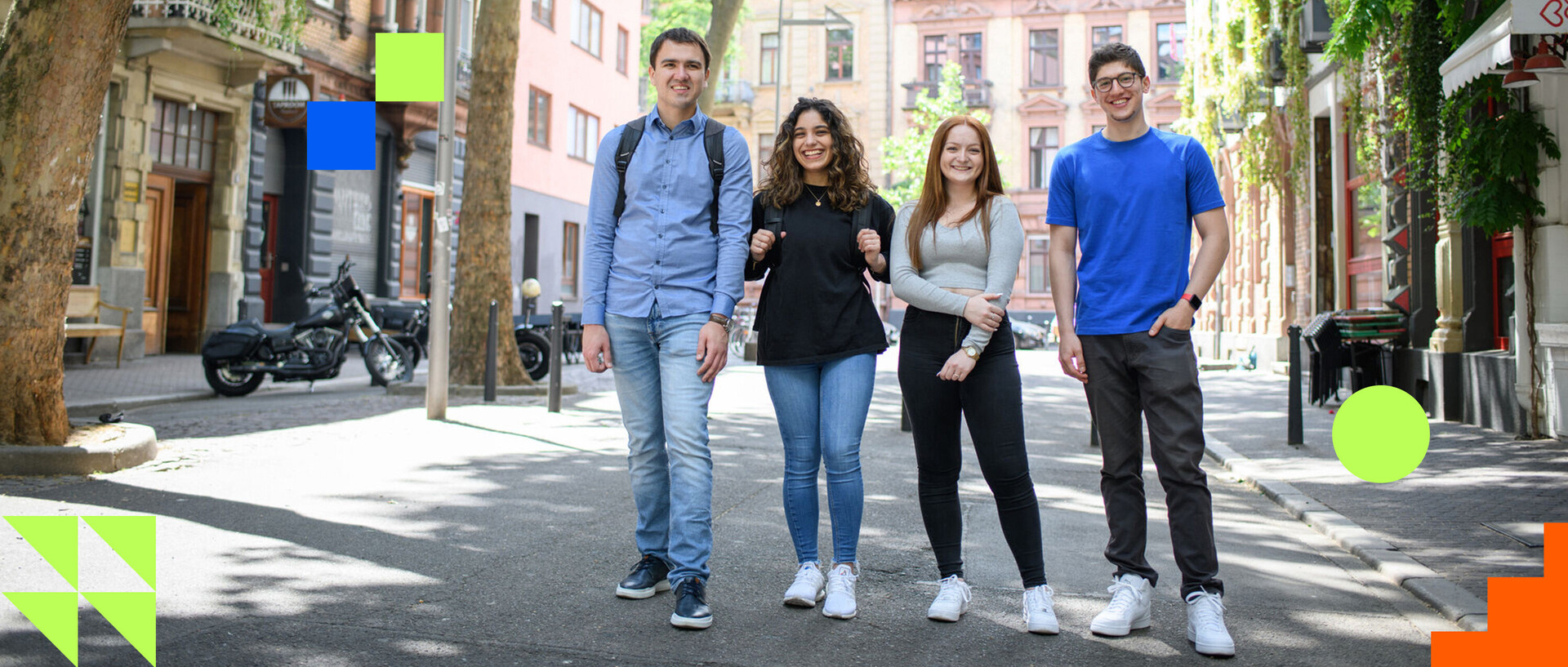 Vier junge Menschen stehen auf einem Platz im Jungbusch und schauen lächelnd in die Kamera.