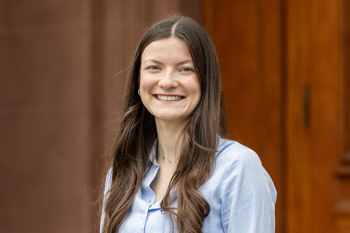 Evelyn Bentz hat lange, dunkelbraune, lockige Haare, trägt eine hellblaue Bluse und lächelt freundlich in die Kamera.