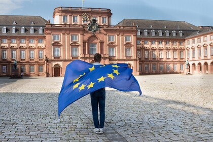 Eine Person mit Europaflagge steht auf dem Ehrenhof des Schlosses.