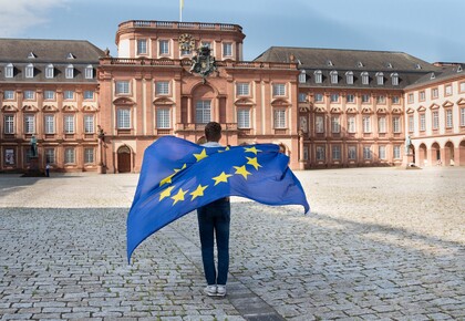 Eine Person mit Europaflagge steht auf dem Ehrenhof des Schlosses.