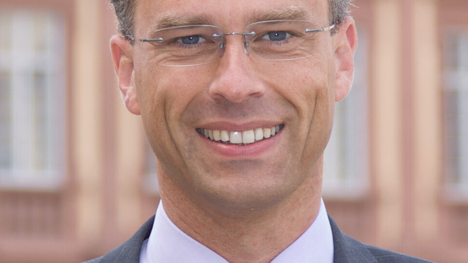 Portrait von Georg Bitter. Er trägt eine lila Krawatte sowuie einen grauen Blazer und steht lächelnd vor dem Schloss.