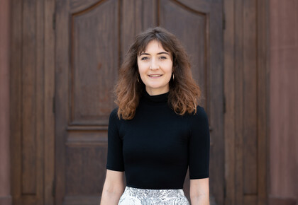 Portrait of Jessica Müller. She is standing in front of a door, waering a black shirt.