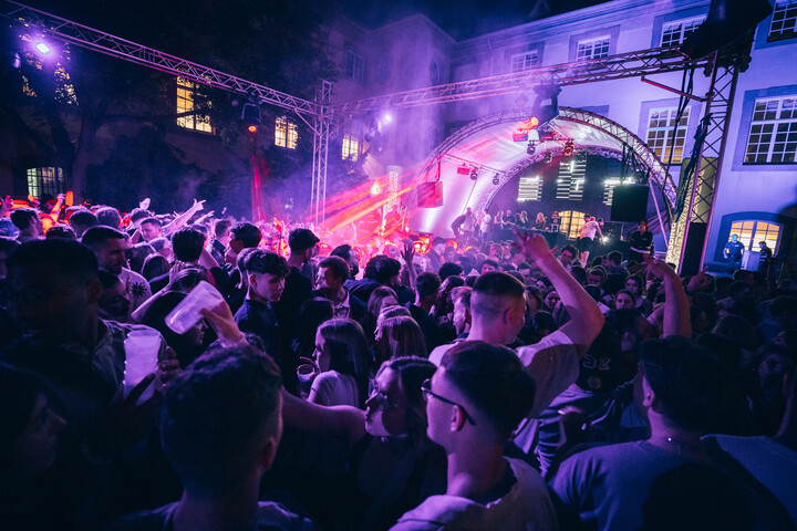 Menschenmenge feiert nachts bei einer Open-Air-Party im Schneckenhof mit Bühne und bunter Beleuchtung.