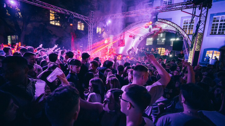 Crowds celebrate at night at an open-air party in the Schneckenhof with a stage and colorful lighting.
