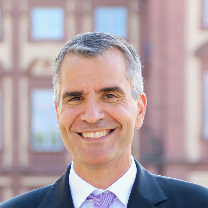 Thomas Fetzer vor dem Schloss im Ehrenhof. Er trägt Anzug, Krawatte und ein weißes Hemd.