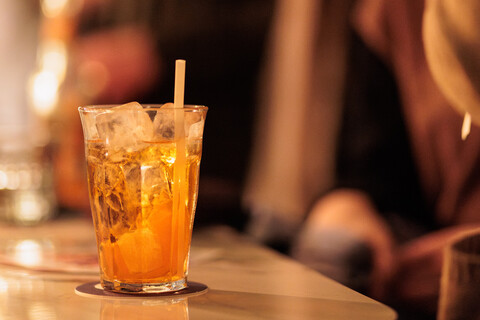 Ein orangefarbenes Getränk in einem Glas mit Eis steht auf einem Bartresen.