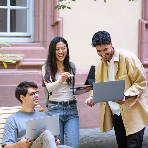 Eine Studentin und zwei Studenten stehen in einem der Schlosshöfe. Alle Drei haben einen aufgeklappten Laptop in der Hand und lachen freudig. Link: Instagram-Post Intensivkurs zur Studienorientierung