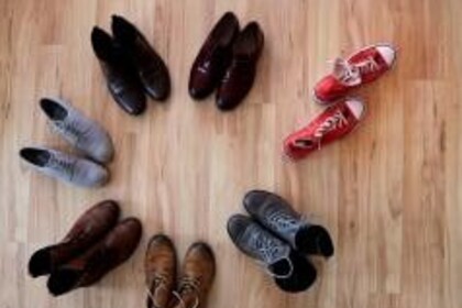 6 Schuhpaare ordentlich im Kreis aufgestellt, ein Paar roter Chucks verlassen den Kreis
